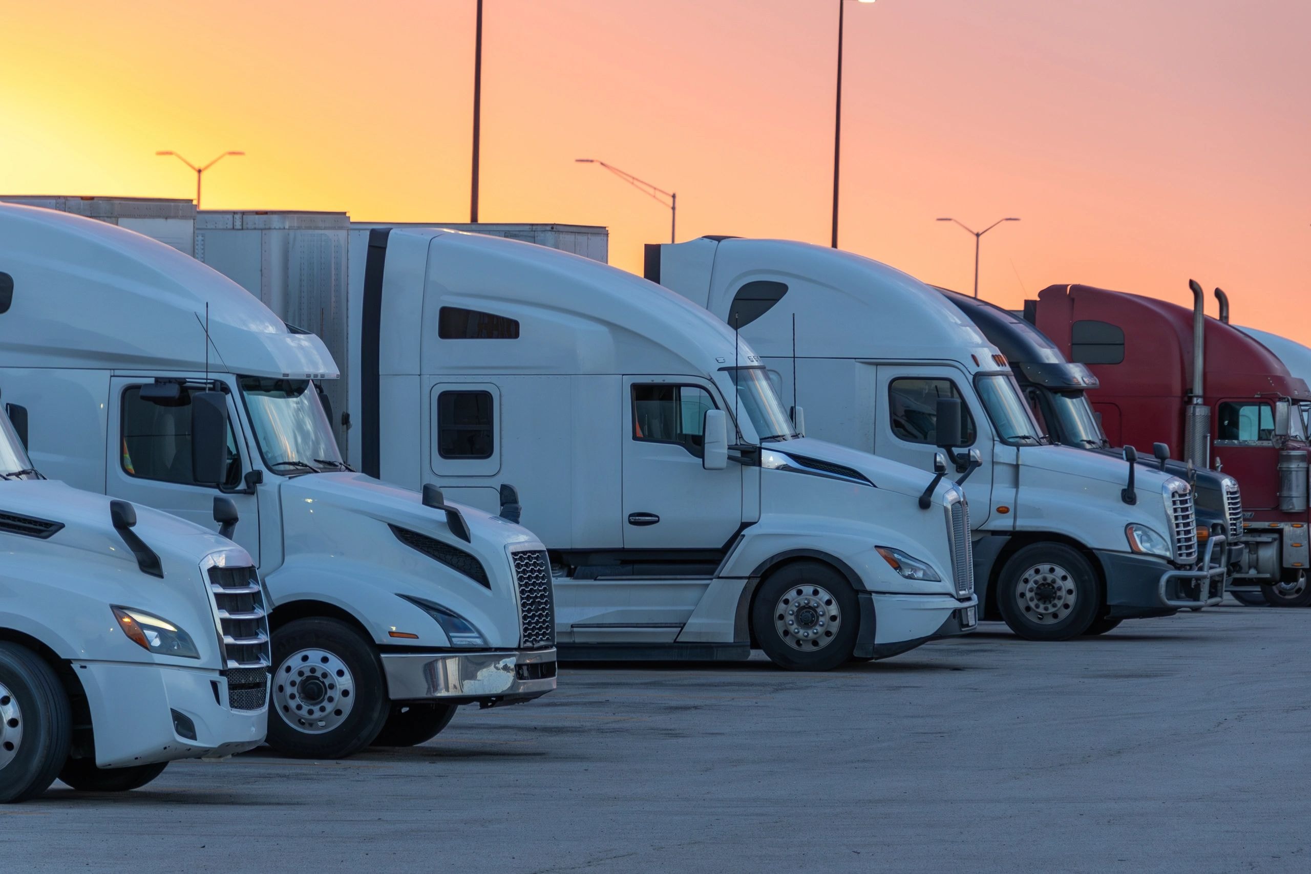 Fleet of semi-trucks parked at depot during golden hour