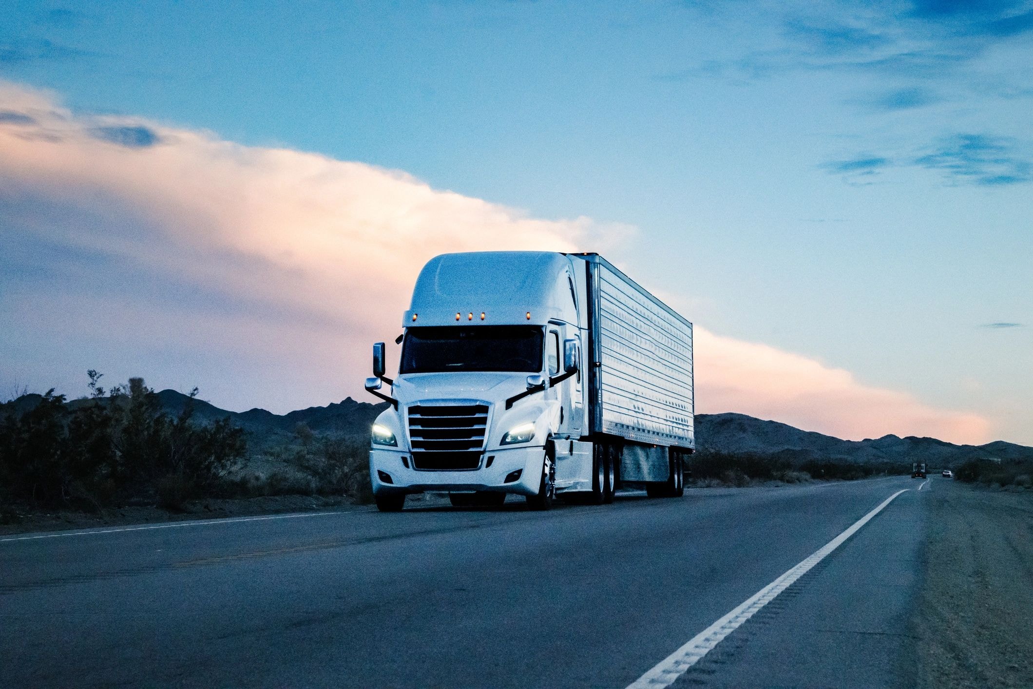White semi-truck on desert highway at golden hour